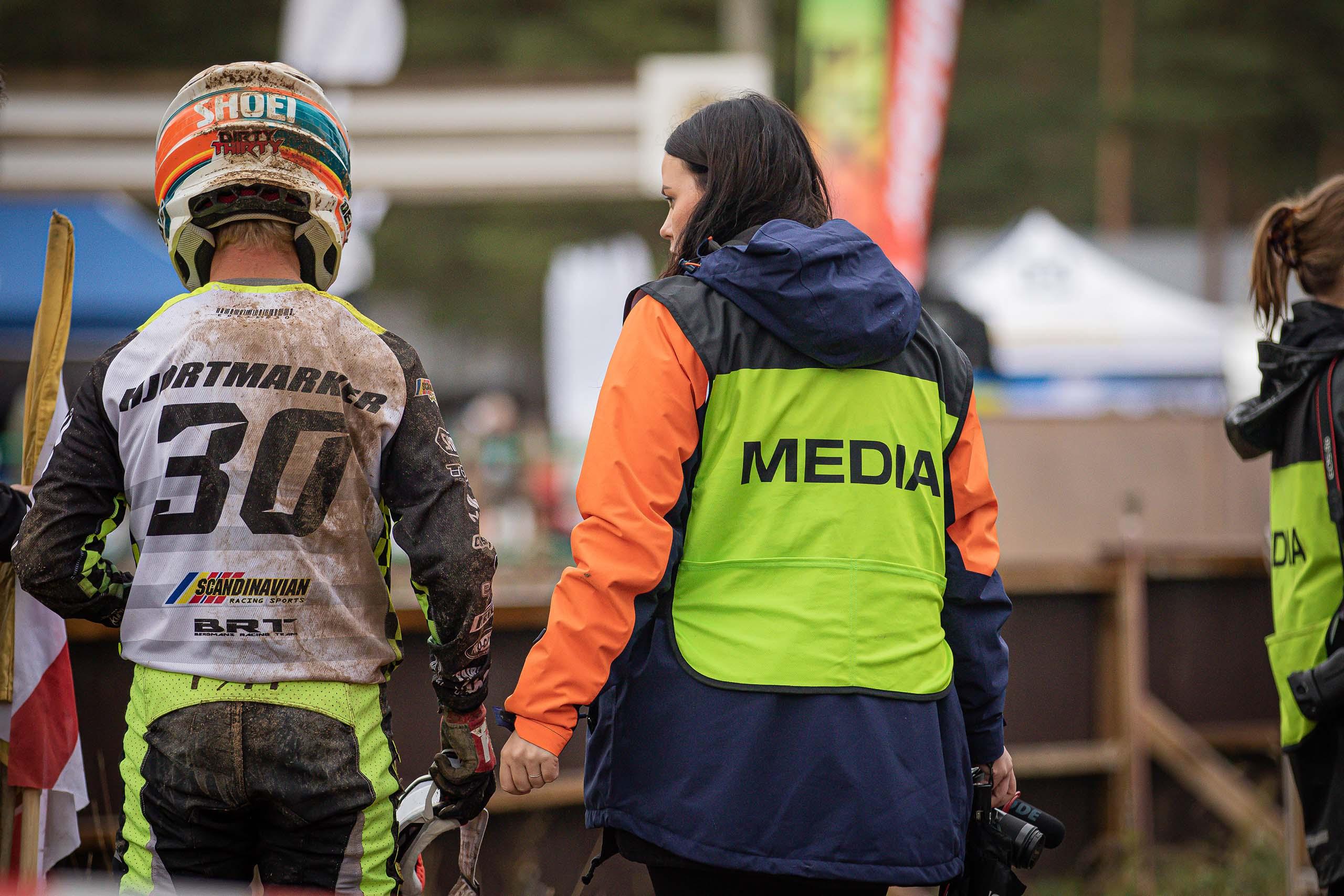 En fotograf med en Svemo mediaväst står och pratar med en förare