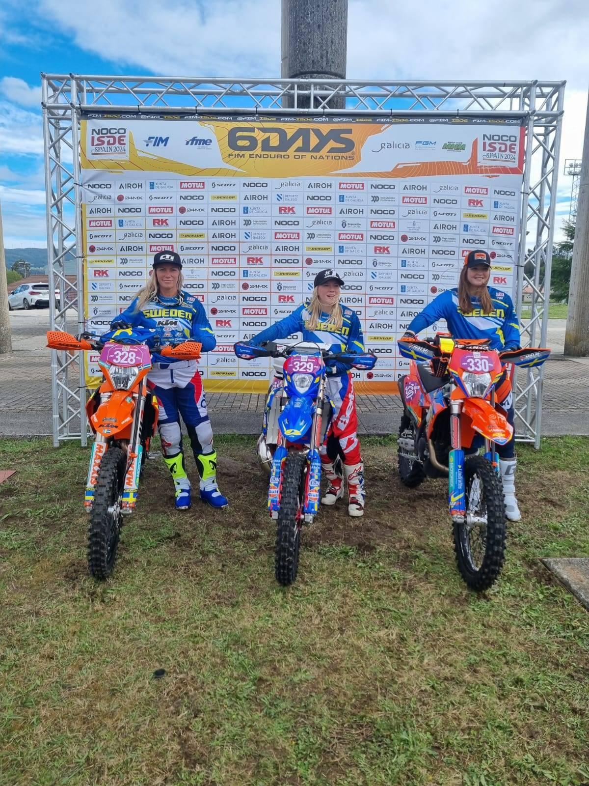 Sveriges Women´s World Trophy Team i ISDE 2024 uppställda brevid varandra och på sidan av sina respektive hojar framför en backdrop med 6Days och sponsorer på.